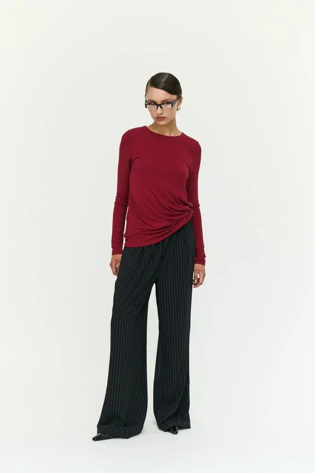 Woman in burgundy long-sleeve top with twist detail and black pinstripe wide-leg pants