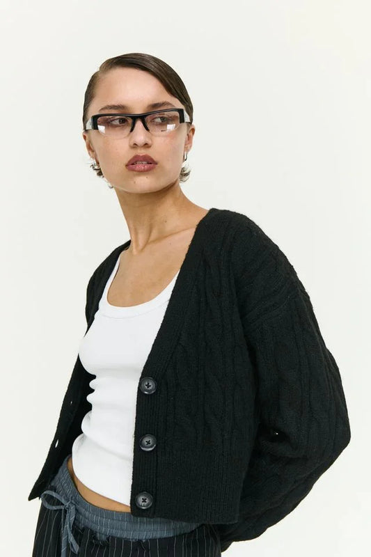 Black cable knit cardigan with buttons, styled over white top and striped pants