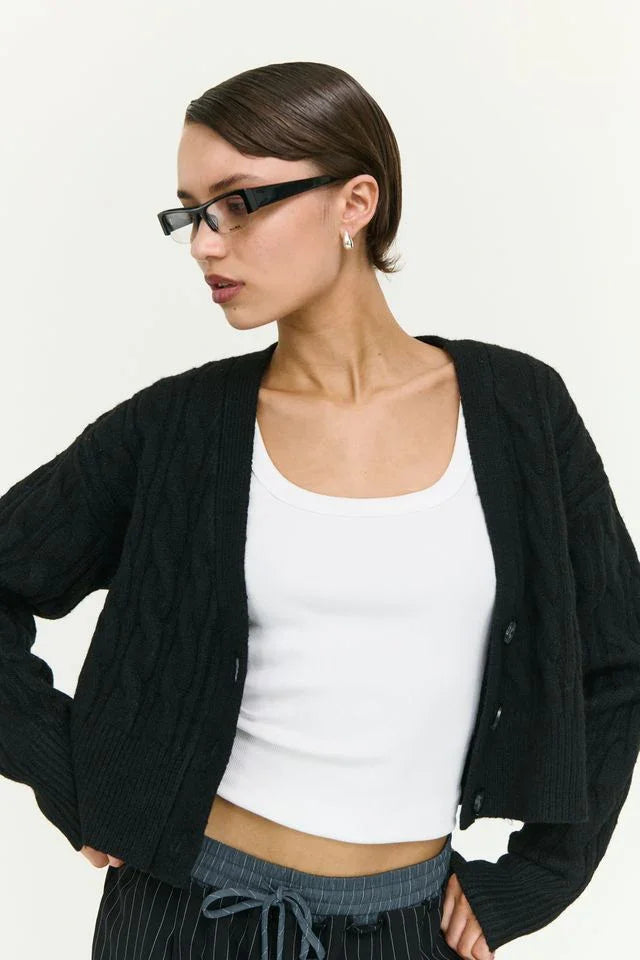 Woman wearing black cable knit cardigan over white crop top, styled with pinstripe pants and sunglasses