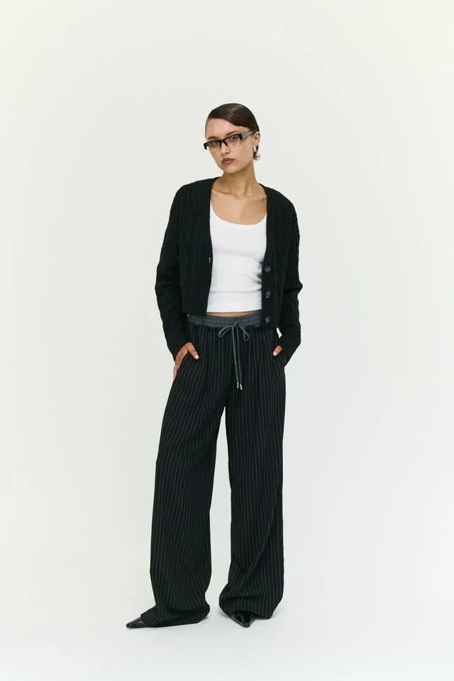 Woman in black pinstripe pants, white top, and cardigan, stylish casual outfit