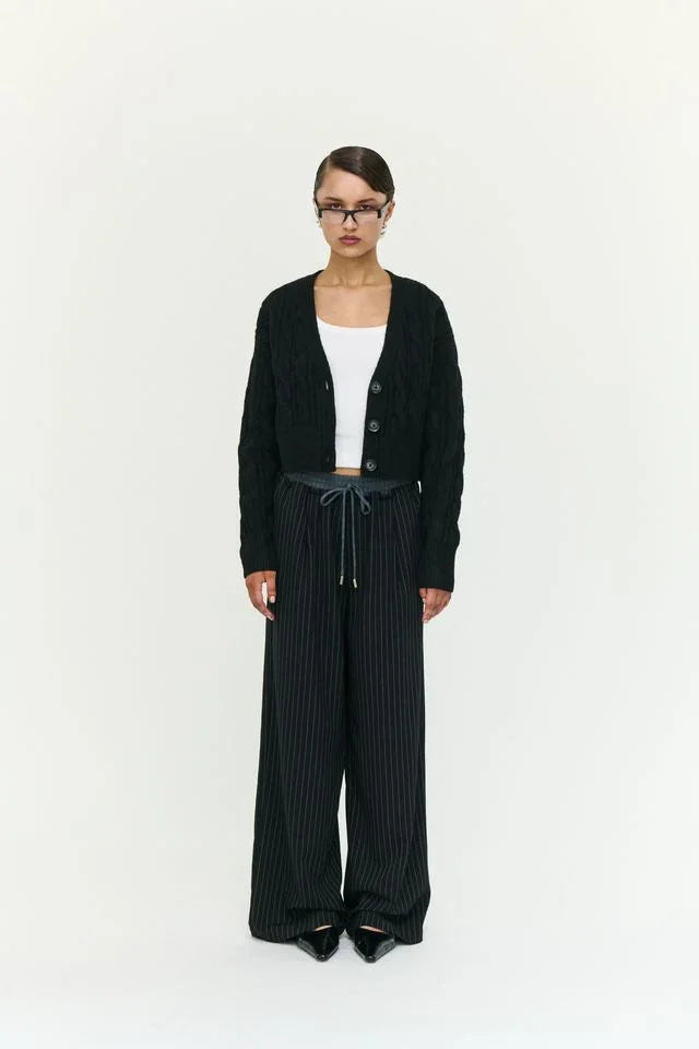 Woman in black cable knit cardigan, white top, and pinstripe wide-leg pants, stylish women's fashion