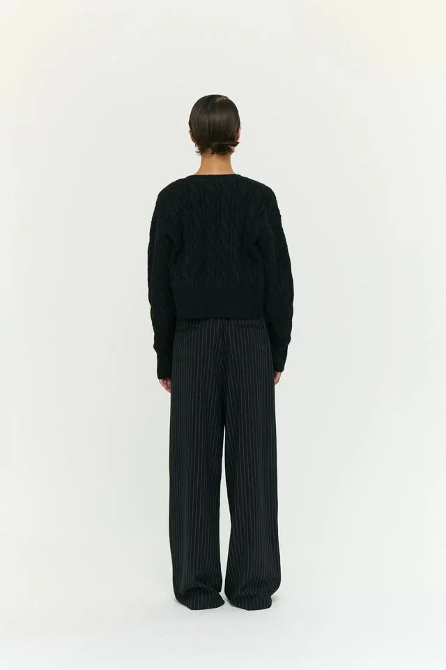 Black cable knit sweater with wide-leg pinstripe trousers, back view